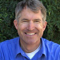 A man with grey hair and blue shirt smiling.