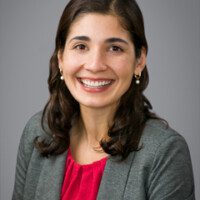 A woman in grey jacket and red shirt smiling.