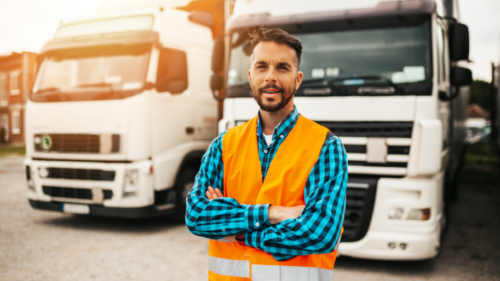 A man in an orange vest standing next to two trucks.