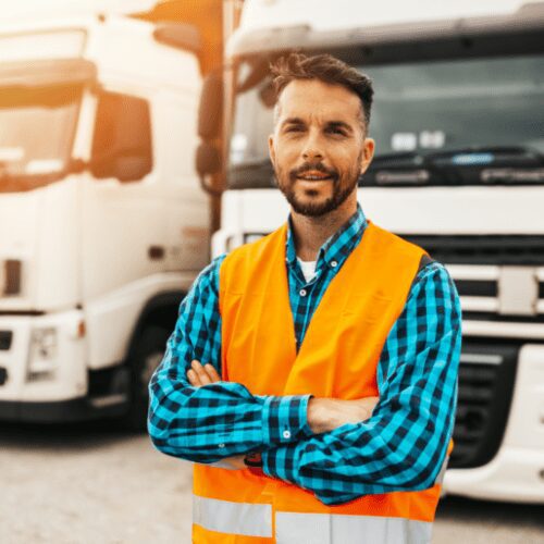 A man in an orange vest standing next to two trucks.